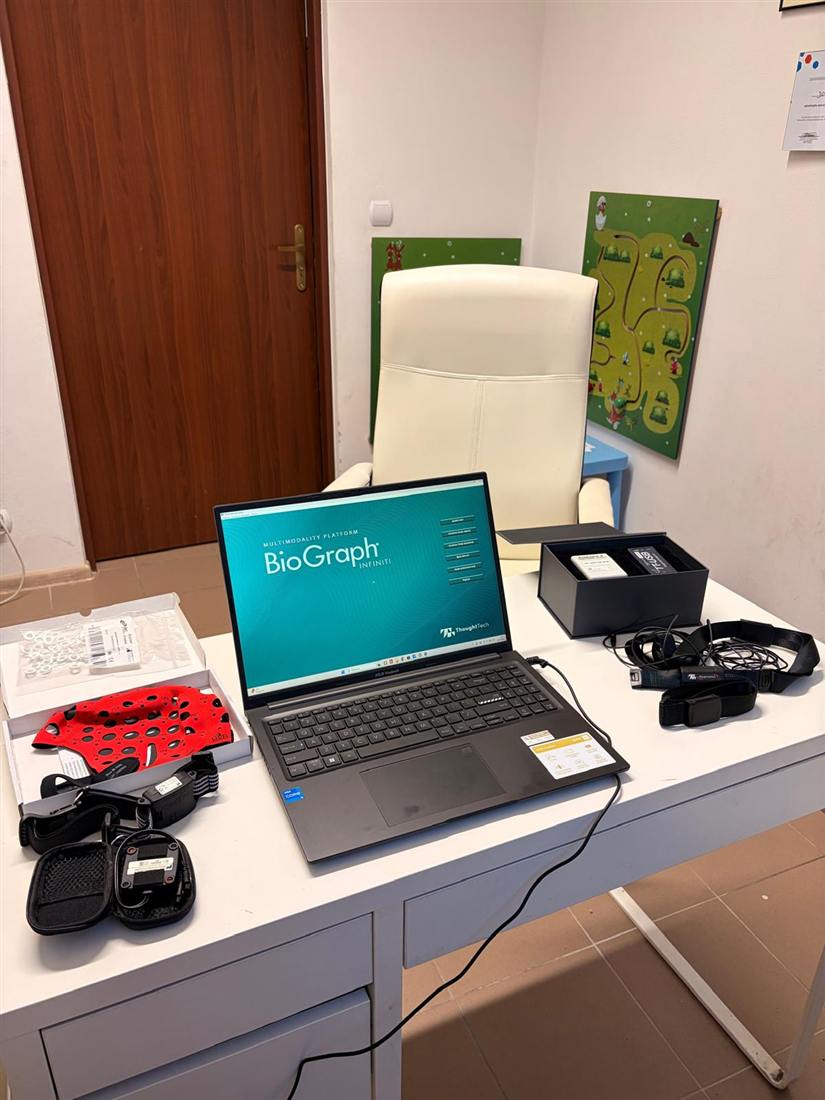 Stanowisko biofeedback w gabinecie: laptop, czepek EEG, czujniki pulsu i pas oddechowy